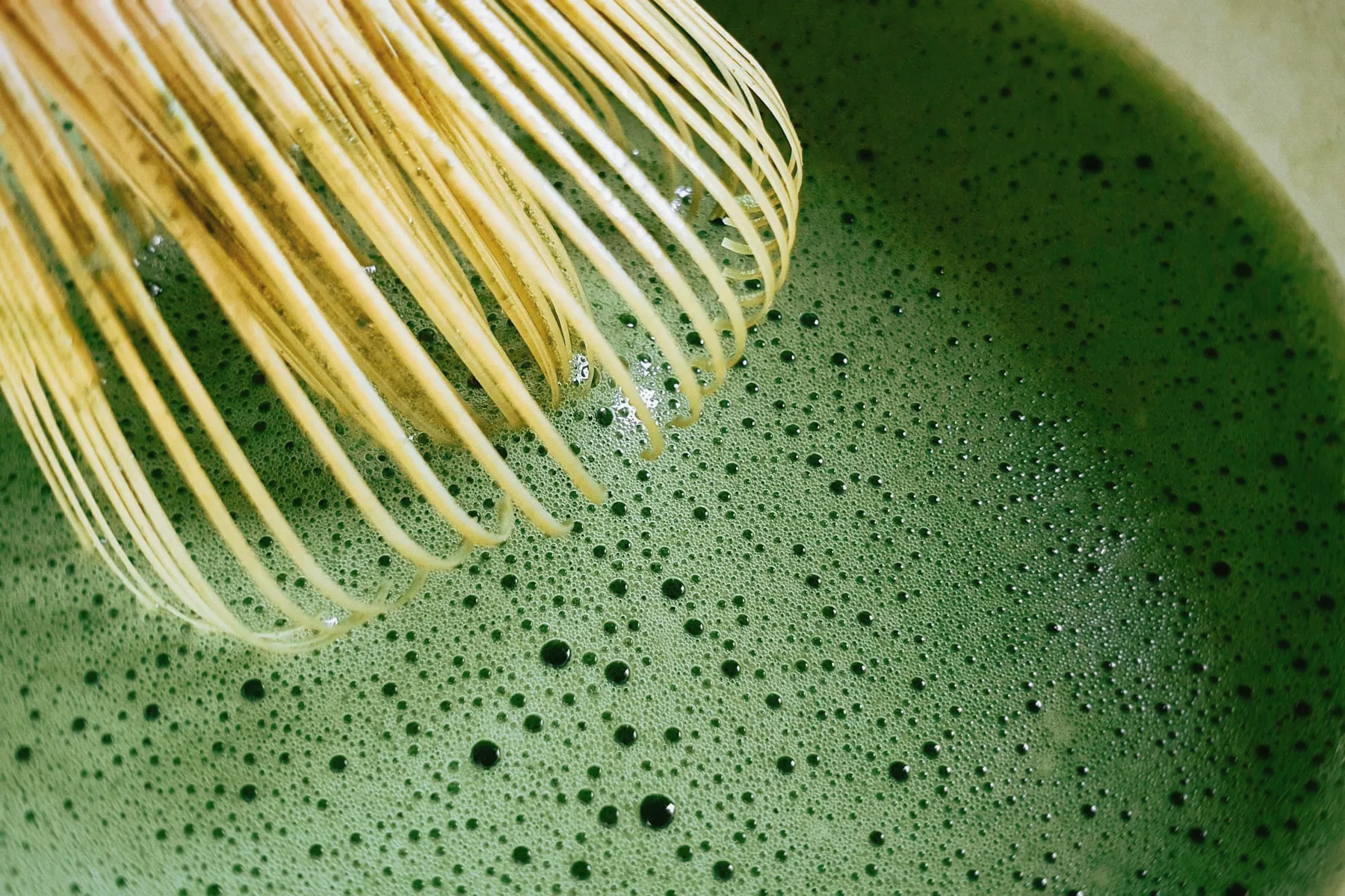 A bamboo whisk resting over freshly whisked matcha